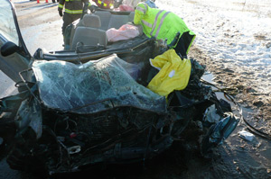 Car crash fire crews inspect a car that is totalled in the snow