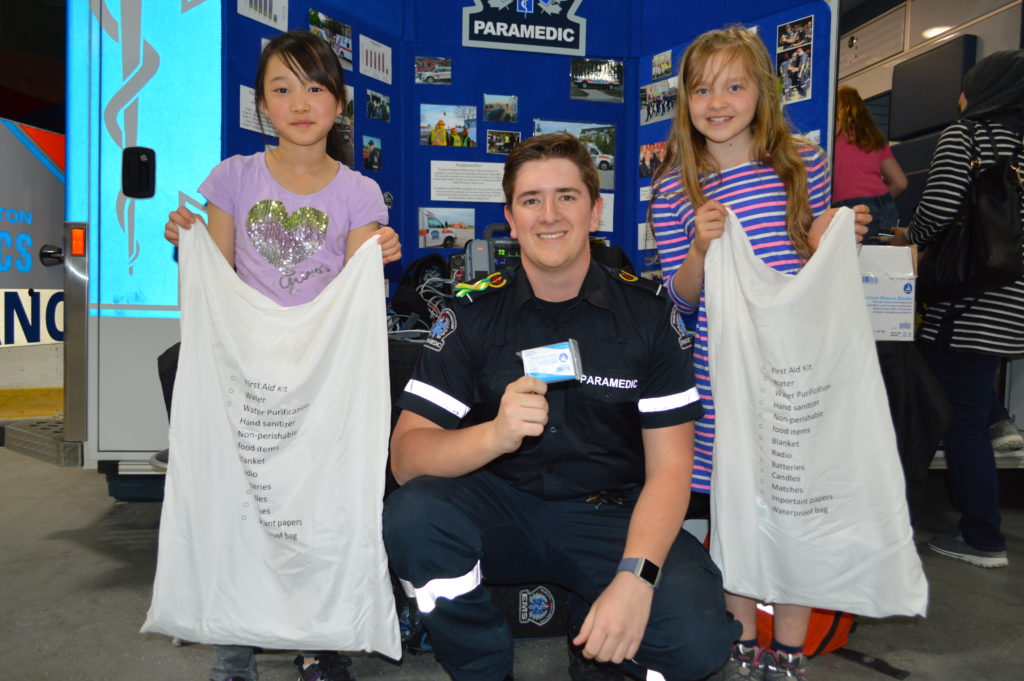 Photo that shows two students holding pillowcases and receiving an emergency blanket from a paramedic.