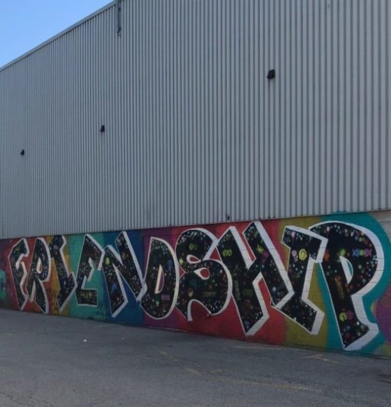 A colour photograph of a building with metal siding at the top and a mural at the bottom that spells FRIENDSHIP.