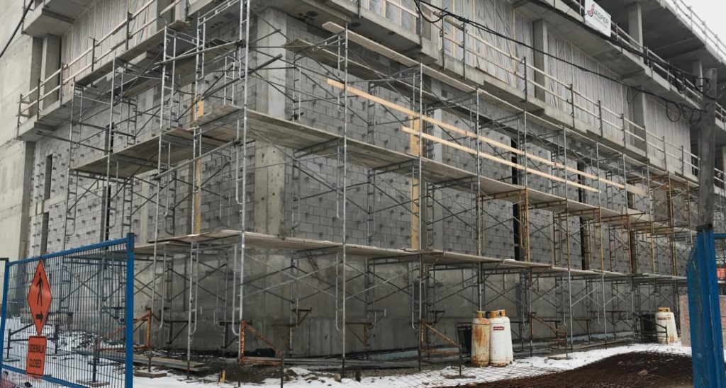 Image taken at the corner of the building shows scaffolding around a grey wall