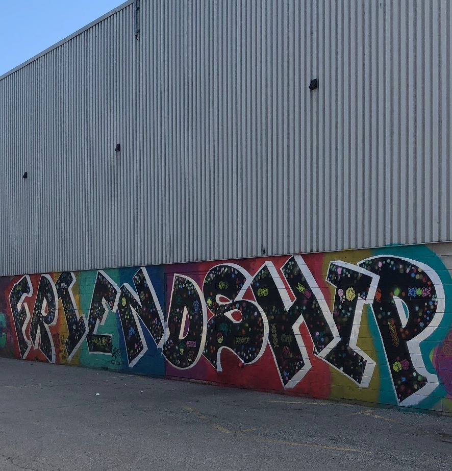 A colour photograph of a building with metal siding at the top and a mural at the bottom that spells FRIENDSHIP