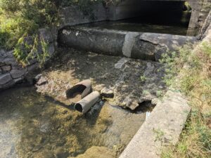 A creek with a sewer pipe exposed and crumbling sanitary pipes.