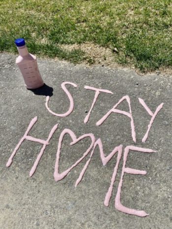 'stay home' painted on a sidewalk with light pink puff paint