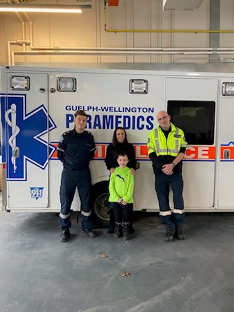 Two paramedics standing with a woman and child in front of an ambulance