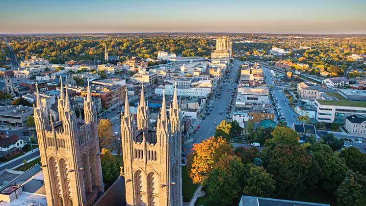 A birds-eye view of Downtown Guelph on a sunny day. The image showcases the Church of Our Lady, downtown businesses and the landscape of Guelph in the distance. 