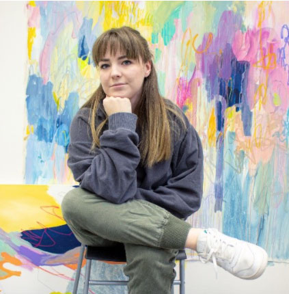 Chanet Desroches seated on a stool in front of a colourful abstract background