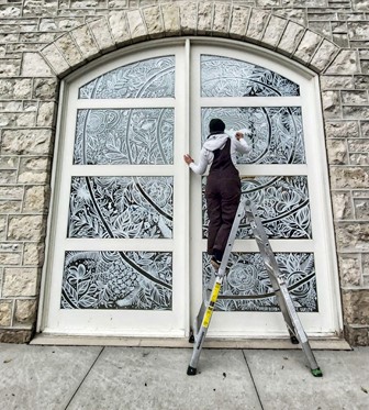 photo of artist Shelby Bohn painting a window 