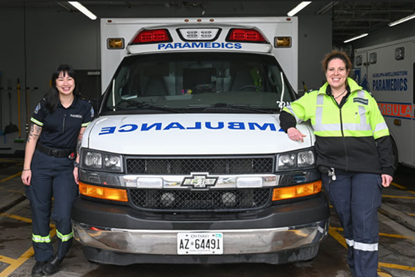 two paramedics: one standing at thr left side of ambulance, the other at the right