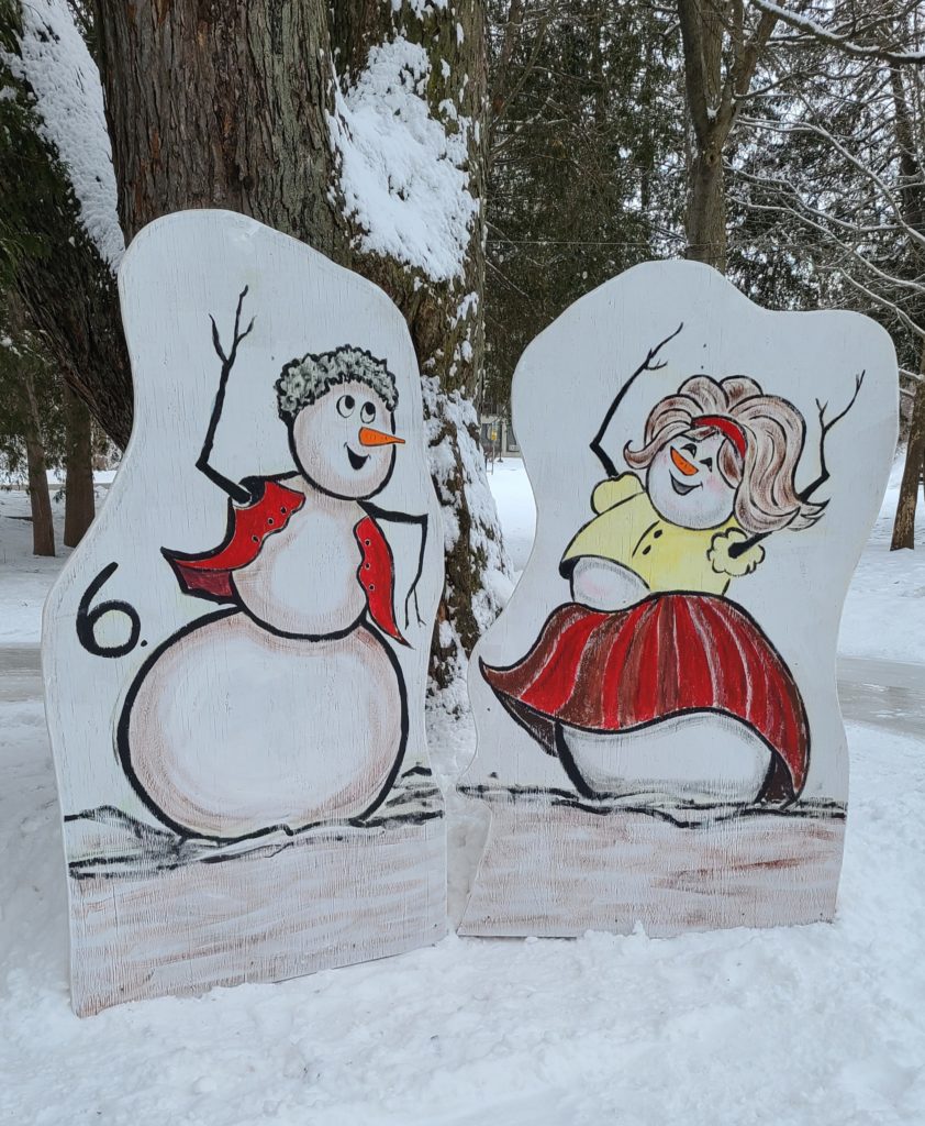 Two snowpeople dance, one wears their shirt open and has short, dark hair and one wears a skirt and top with lighter, longer hair.