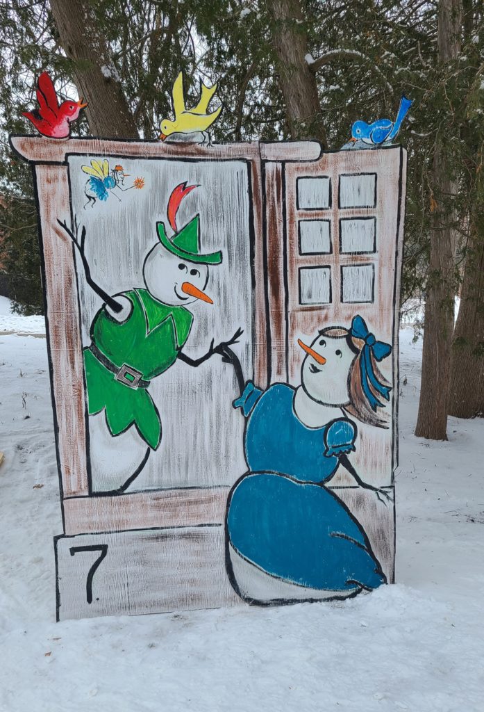 One snowperson wearing a blue dress is at a window, and another hovers outside in the air wearing a tunic and cap. A tiny fairy flies in the air.